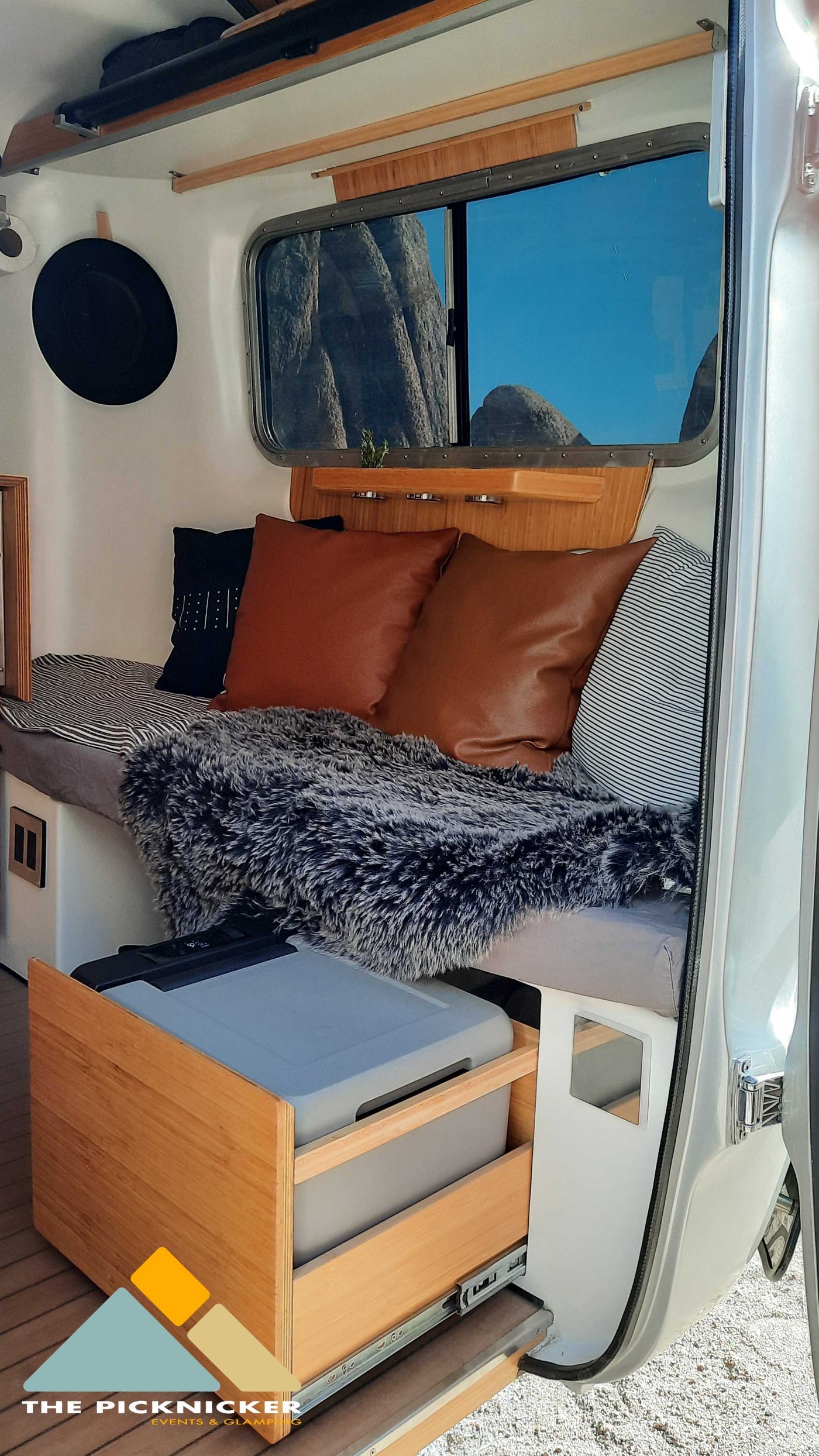 Inside a cozy RV rental: bench seating, faux fur throw, scenic window view, and smart pull-out fridge. — photo 12