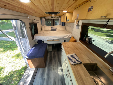 Cozy RV rental interior, showcasing a comfortable bed, compact kitchen, and warm wood accents. Perfect for a road trip.