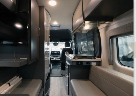 Modern RV rental interior, showcasing a living area, kitchen counter, TV, and the driver's cockpit.
