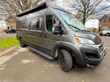 This sleek, dark gray camper van with all-terrain tires and an awning looks like an excellent RV rental option.