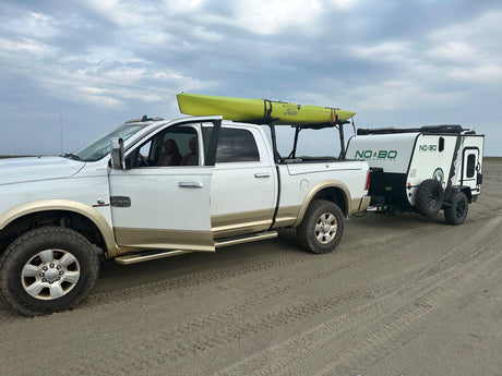 White Ram truck with kayak tows a NO BO RV on sand.