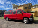 A red van, reminiscent of an RV rental, parked alongside a yellow building under blue, cloudy skies.