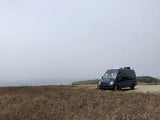 A dark rv rental camper van sits on a brown field under a foggy sky, ready for a road trip or serene van life.
