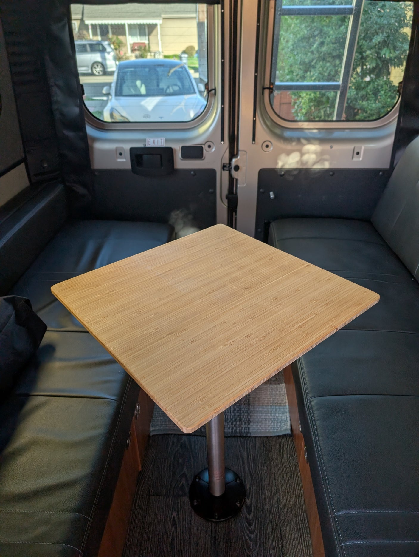 Cozy rv rental interior: bamboo table, black benches, and street view from the windows with an exit sign.