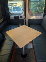 Cozy rv rental interior: bamboo table, black benches, and street view from the windows with an exit sign.