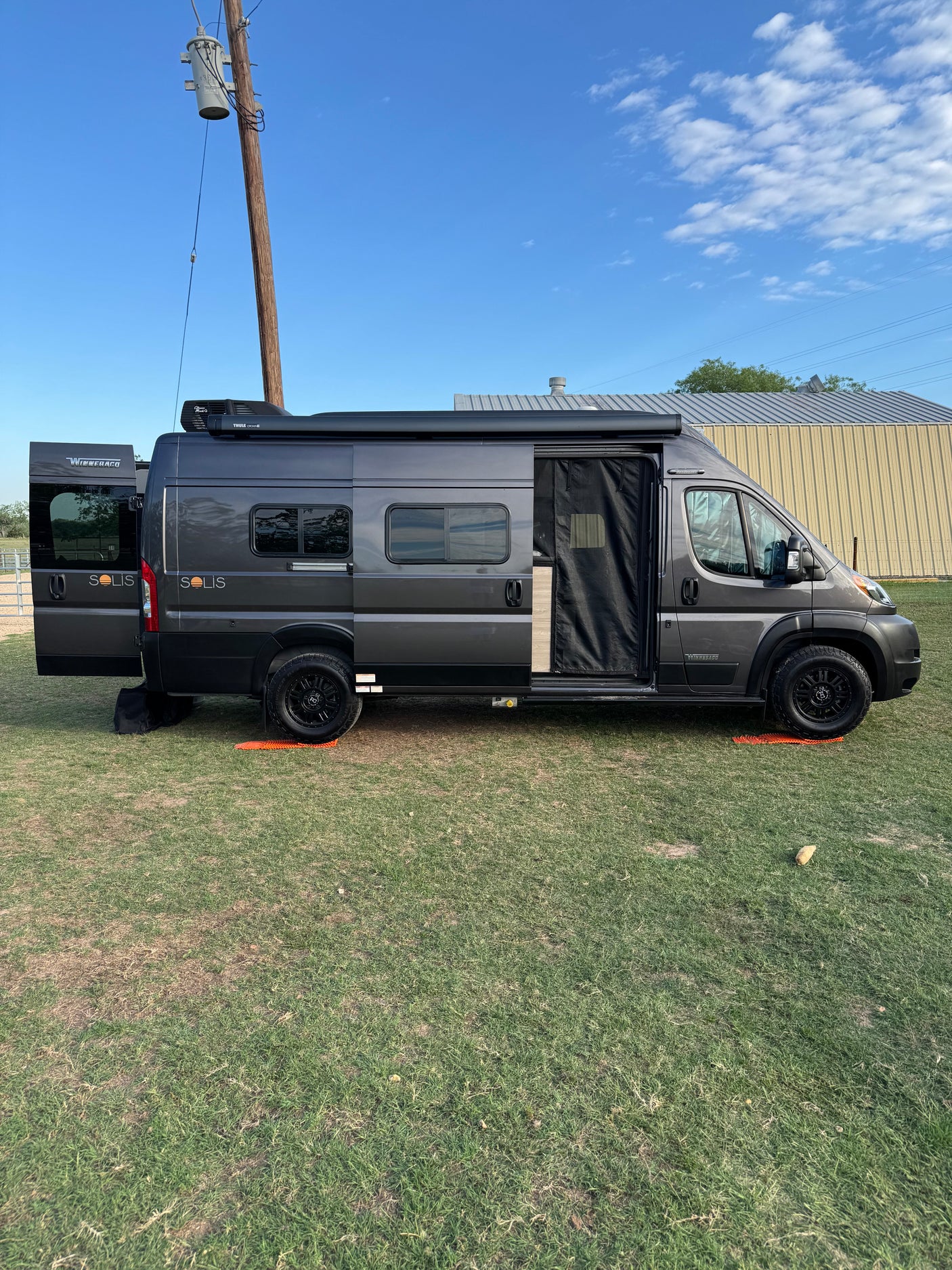 Dark gray Winnebago Solis RV rental parked on grass with doors open and awning out, ready for adventure. Ideal for camping.