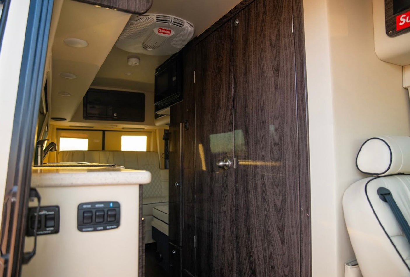 Step inside this RV rental: a modern interior with a functional kitchenette, ample dark wood storage, and rear lounge.