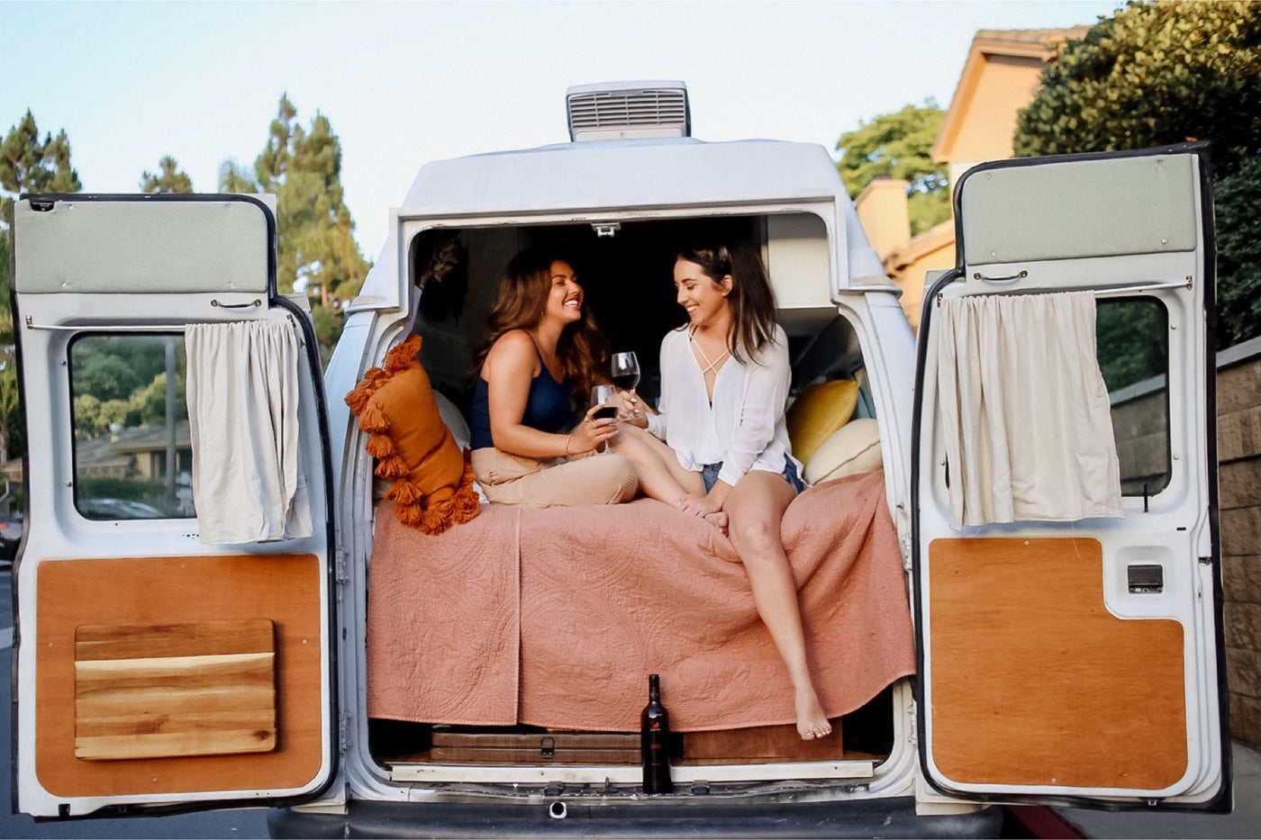Two friends relax with wine inside a cozy RV rental van, showcasing comfortable travel. Ideal for a serene getaway. — photo 7