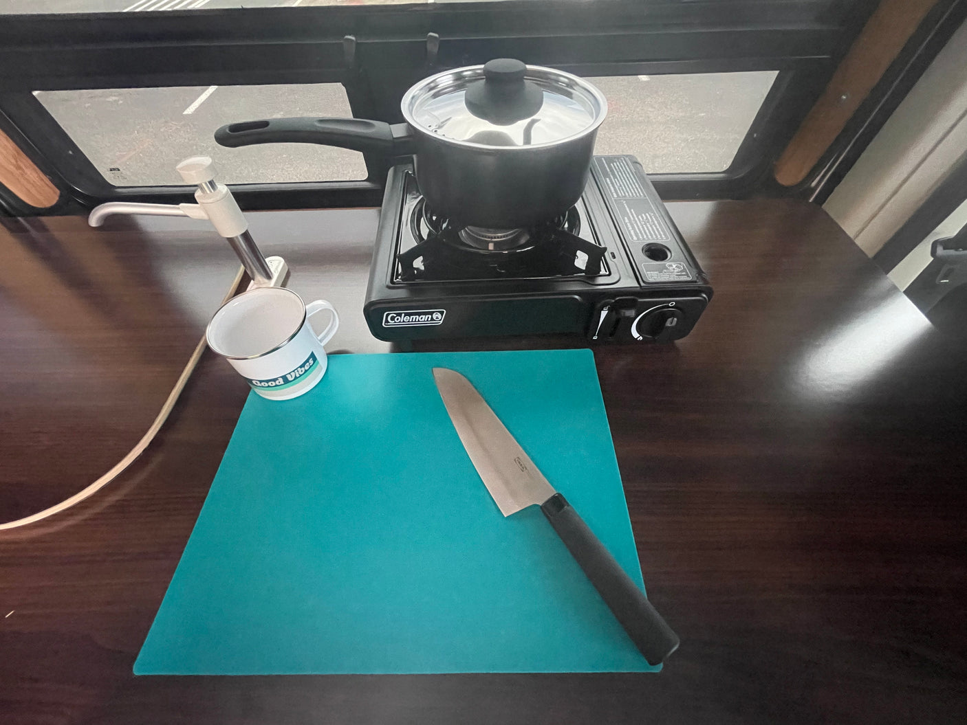 RV rental kitchen essentials: portable stove with pot, sink, cutting board, and knife on a wooden counter.