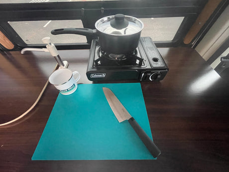 RV rental kitchen essentials: portable stove with pot, sink, cutting board, and knife on a wooden counter.