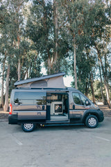 Explore in this Tofino RV rental! Gray pop-top camper van with open door, showing compact interior setup.