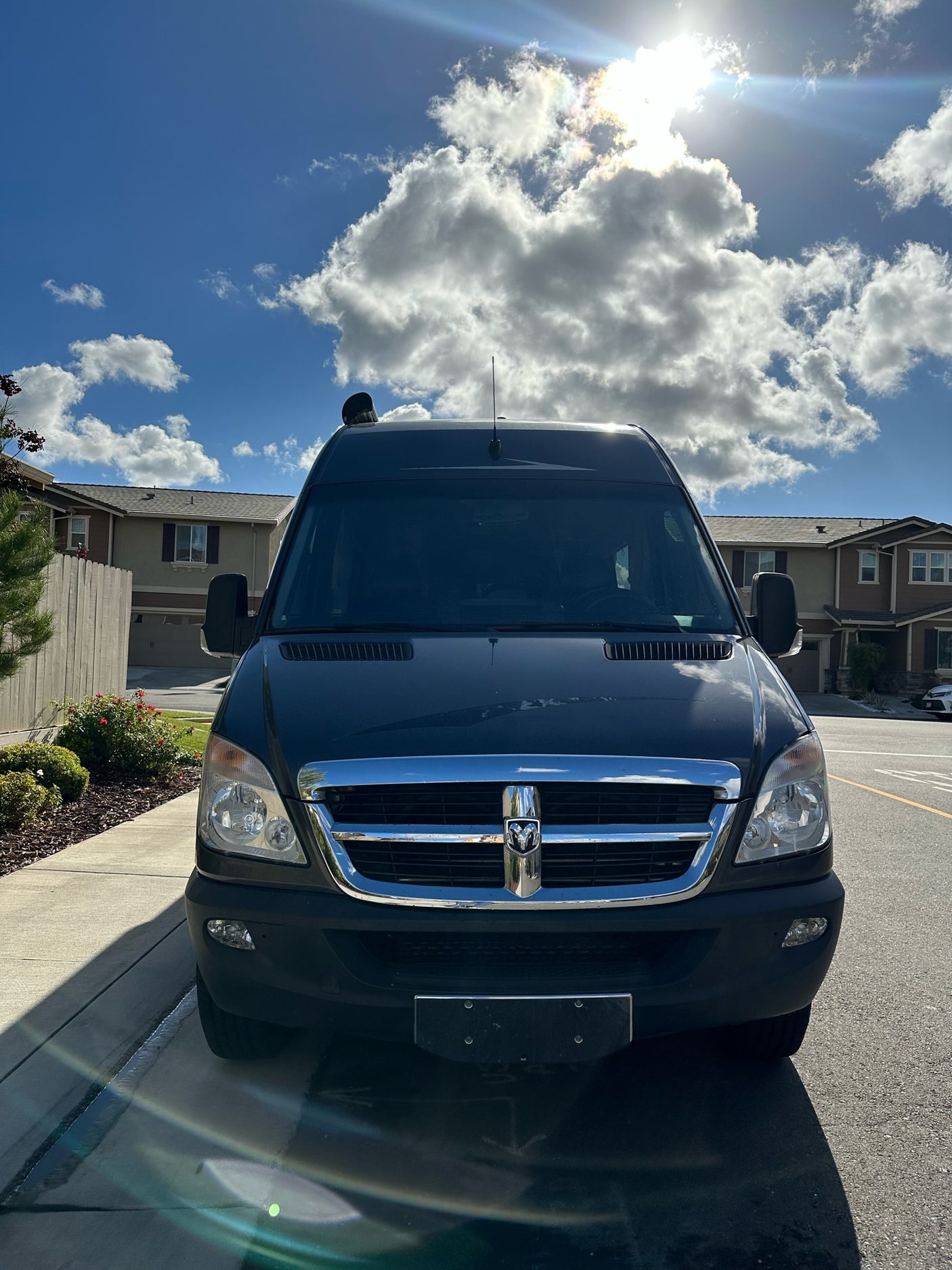 Sleek black RV rental van with Dodge emblem, ready for adventures. Parked on a sunny residential street.