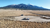 RV rental, camper van, and travel trailer set up for camping in a scenic dry landscape below snow-capped mountains.