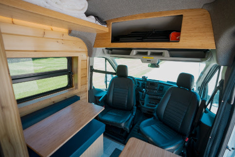 Spacious RV rental interior featuring wood-paneled walls, a dining area with a window and bench, plus front seats.