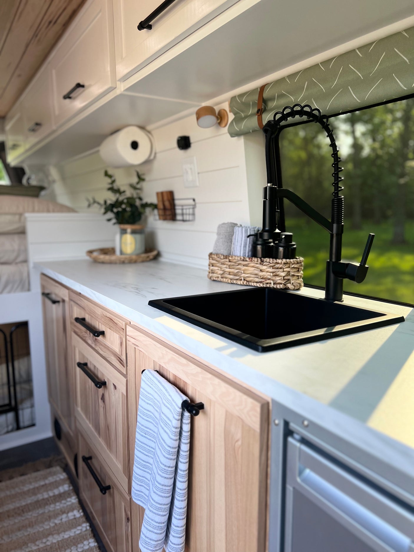 Stylish RV rental kitchen with black sink, pull-down faucet, light wood cabinets, and white countertops.