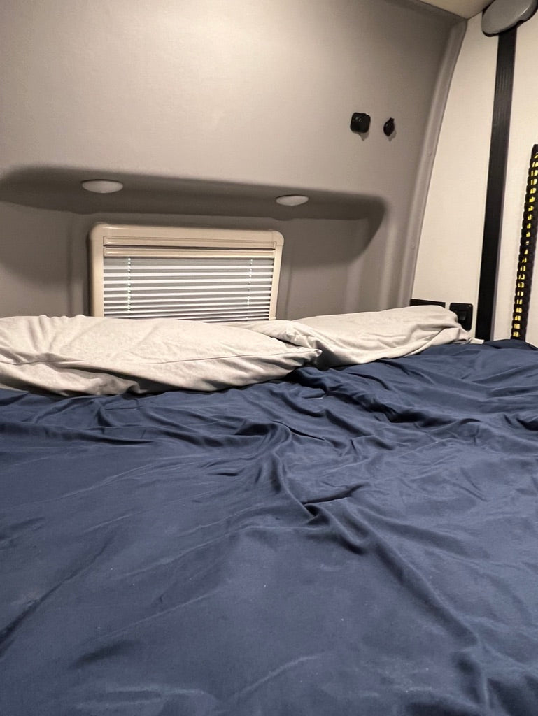 Cozy RV rental bedroom interior with a comfortable bed, pillows, and a window with blinds.
