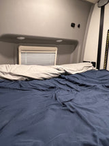 Cozy RV rental bedroom interior with a comfortable bed, pillows, and a window with blinds.