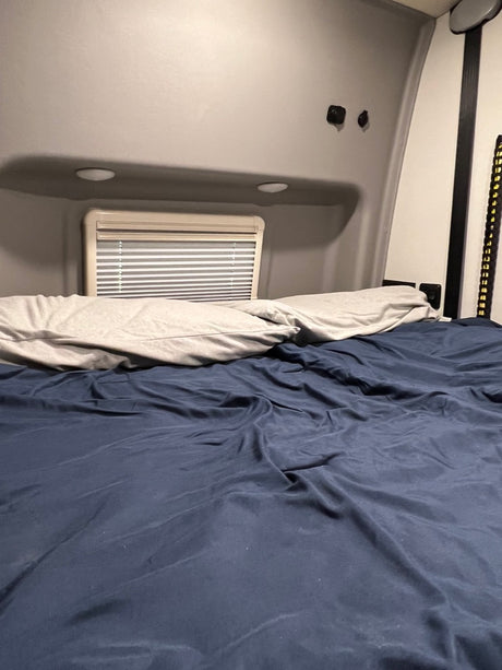 Cozy RV rental bedroom interior with a comfortable bed, pillows, and a window with blinds.