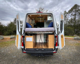Explore in comfort! This RV rental offers a well-appointed camper van interior, featuring a bed & storage, seen with open doors.