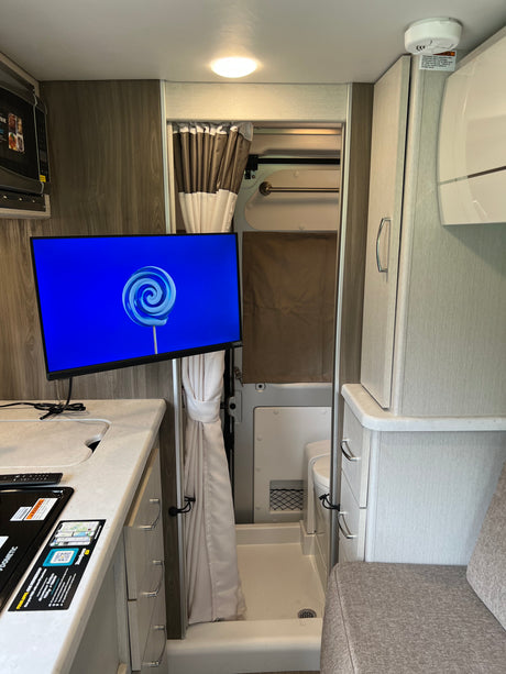 Explore this RV rental's interior: compact kitchen with microwave, TV, wet bath with shower, and comfy seating.