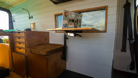RV rental interior: Bright camper van mobile office setup with a laptop, window view, wooden storage, and seating.