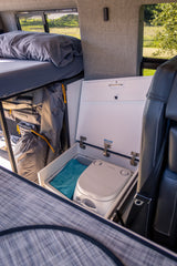 Compact RV rental interior: bed, organized storage, and a discreet Dometic portable toilet. Adventure ready.