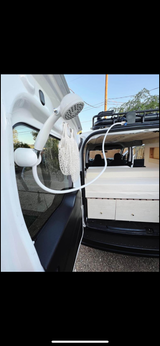 Portable outdoor shower setup on a white camper van, revealing the interior bed and storage. Ideal for your next RV rental adventure.