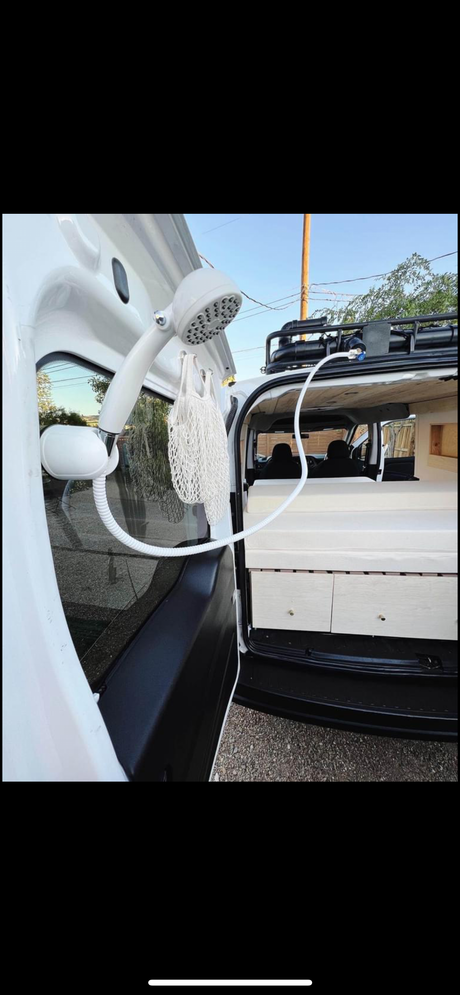 Portable outdoor shower setup on a white camper van, revealing the interior bed and storage. Ideal for your next RV rental adventure.