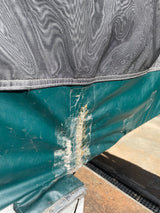 Close-up of a damaged RV rental: Worn green vinyl panel below a mesh screen, patched with clear tape showing poor repair.