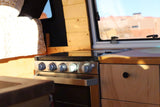 RV rental interior: a modern stainless steel stove/oven, wooden cabinetry, and a cozy bed, perfect for travel.
