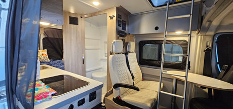 This RV rental interior offers a kitchen area, compact bathroom, bed, and flexible seating with an upper bunk ladder.