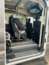 Spacious RV rental interior featuring a child car seat and versatile seating on floor rails. Overhead screen and storage optimize comfort.