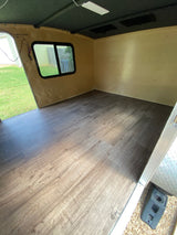 Renovated RV interior showcasing new wood-look flooring, light walls, a dark ceiling, and a window. Ideal for rv rental.