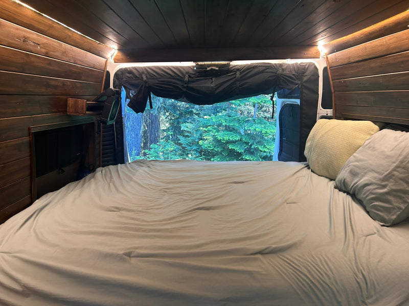 Relaxing rv rental bed in a wood-paneled camper van, illuminated by LED lights with a serene view of green trees. — photo 11