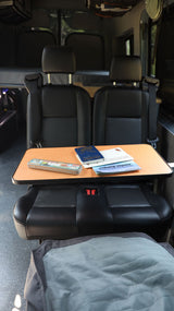 Inside an RV rental: two black seats, a pull-out table with a National Parks Passport, and Junior Ranger booklets.