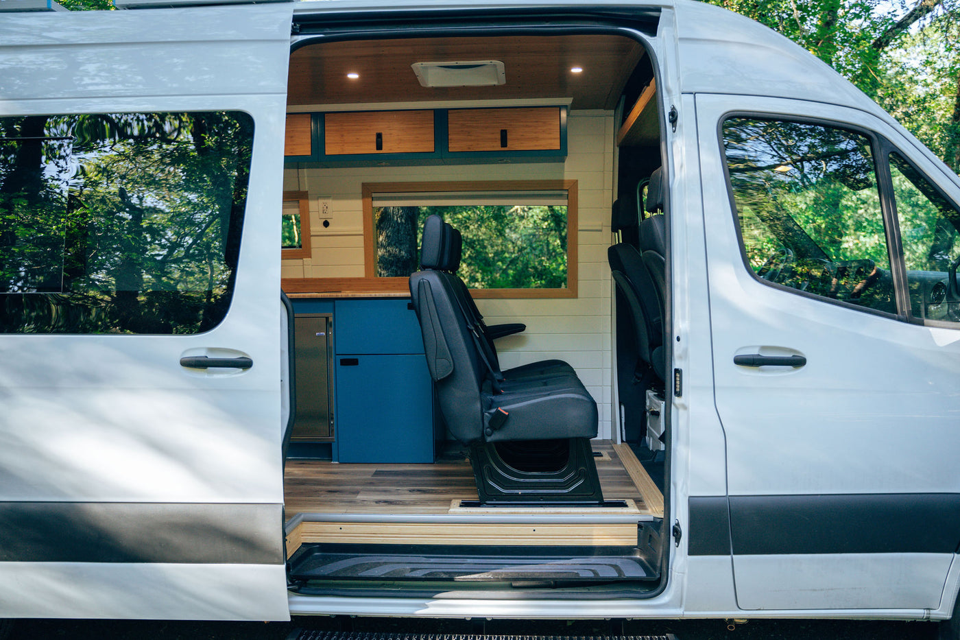  parked on a dirt path in a sunny green forest.|Explore this custom rv rental interior! Featuring a compact kitchen — photo 2