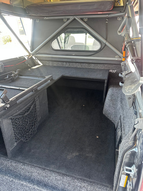 Carpeted truck bed interior with custom storage and topper, ready for your RV rental overlanding adventures.
