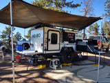 An RV rental teardrop camper, with an awning, truck, and dog, creates a perfect outdoor living space for adventure camping.