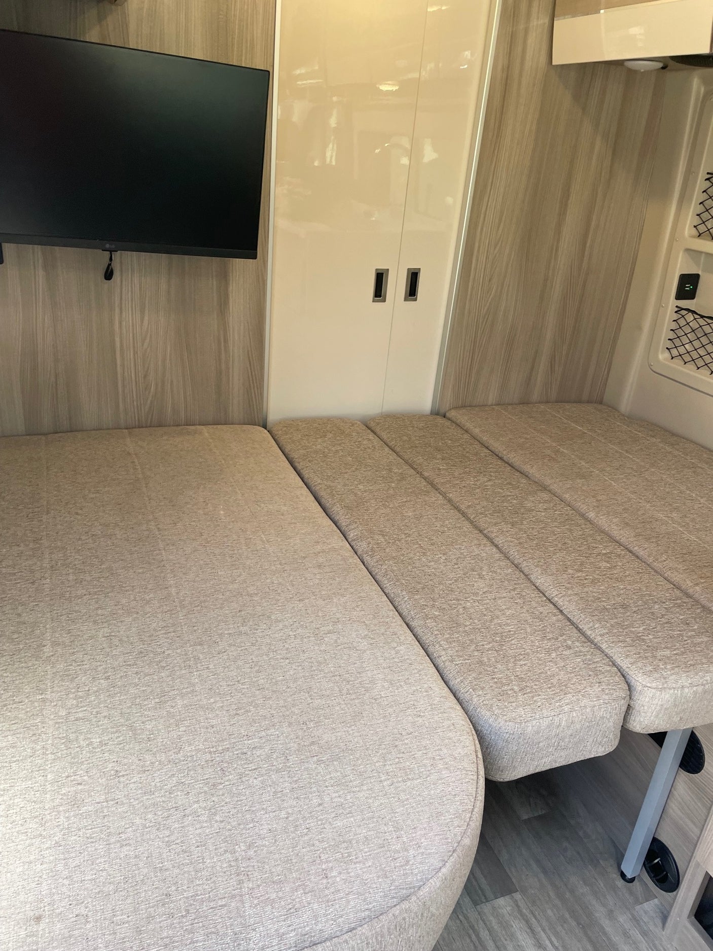 Spacious RV rental interior featuring a convertible bed/seating area, wall-mounted TV, and light wood finishes.