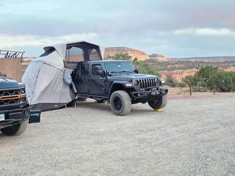 An RV rental overlanding setup: a black Jeep Gladiator with a rooftop tent and annex, parked in a desert landscape.