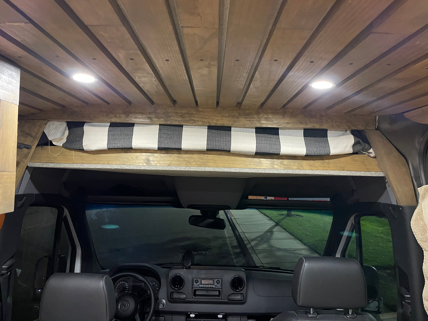 Spacious RV rental van interior featuring a slatted wood ceiling, bright lights, and a checkered curtain above the dash.