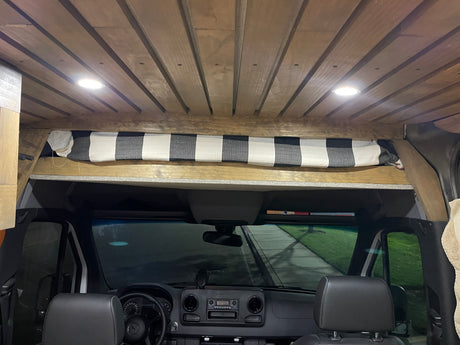 Spacious RV rental van interior featuring a slatted wood ceiling, bright lights, and a checkered curtain above the dash.
