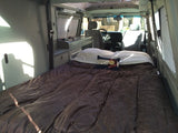Spacious RV rental bed setup with brown comforter & Colorado pillow. Shows built-in storage/kitchen area.