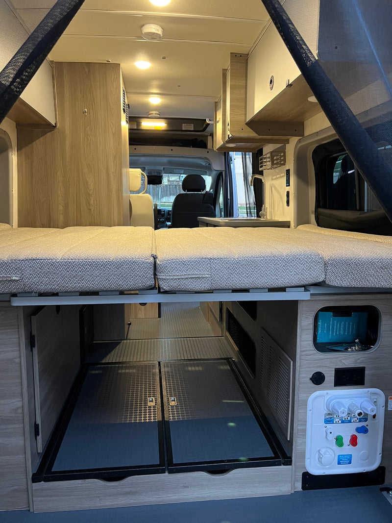 Inside an RV rental: view of the bed, under-bed storage, and utility panel in a camper van. Designed for travel comfort. — photo 9