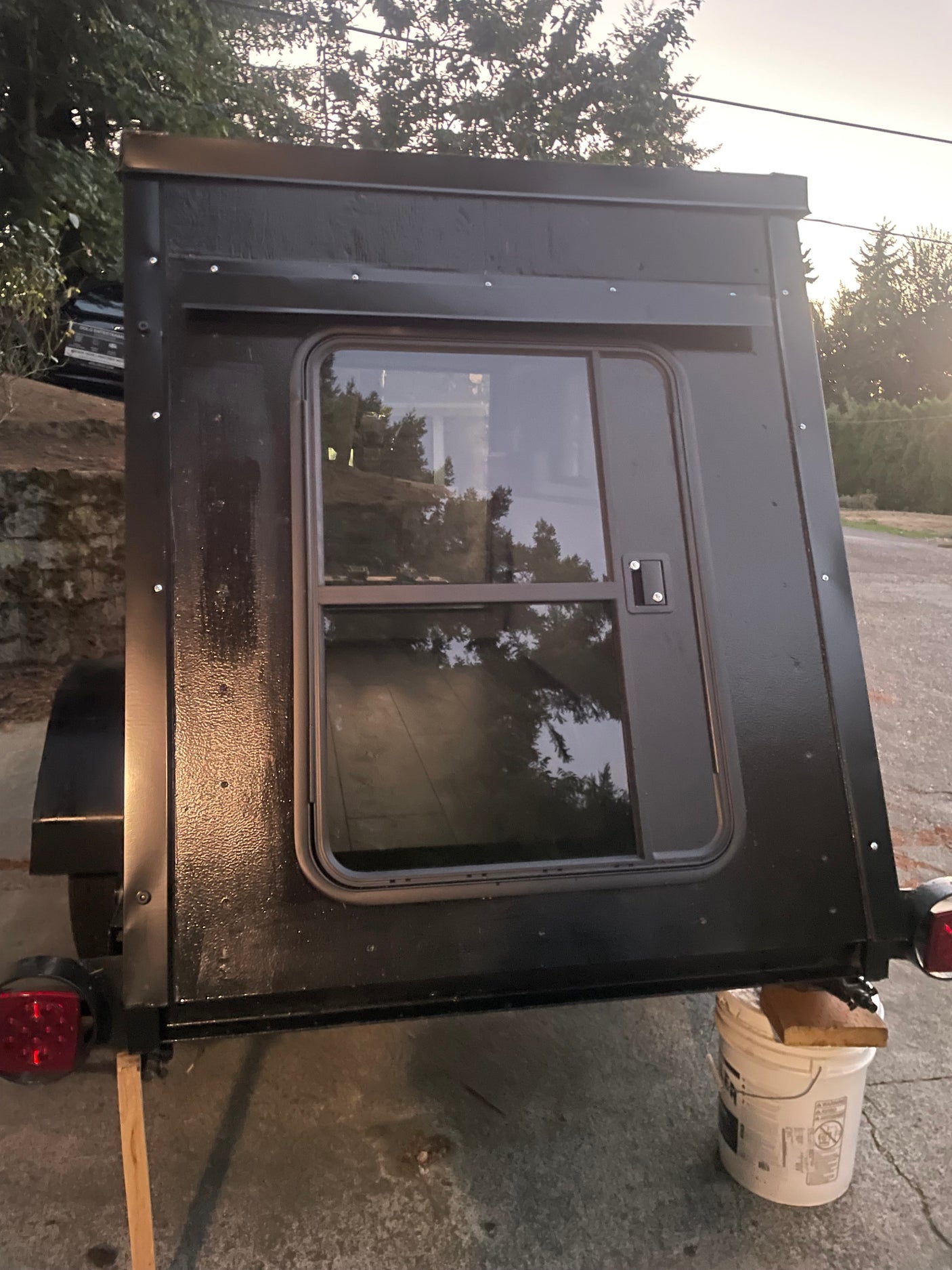 Exterior of a black DIY camper trailer, featuring a side window and textured finish. Could be a unique option for an RV rental.