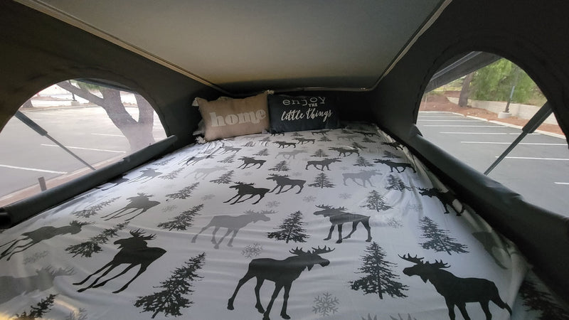 Cozy rv rental pop-top camper bed with moose bedding and pillows. Outside, a parking lot view. — photo 10