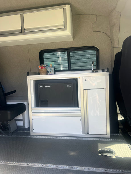 RV rental interior featuring a modular kitchen unit with a Dometic fridge, sink, and overhead storage cabinets.