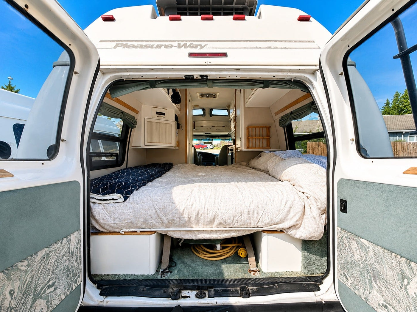  two camping chairs & table on a driveway next to a house.|Relax under the awning of your white camper van RV rental. Perfect for a cozy road trip — photo 7