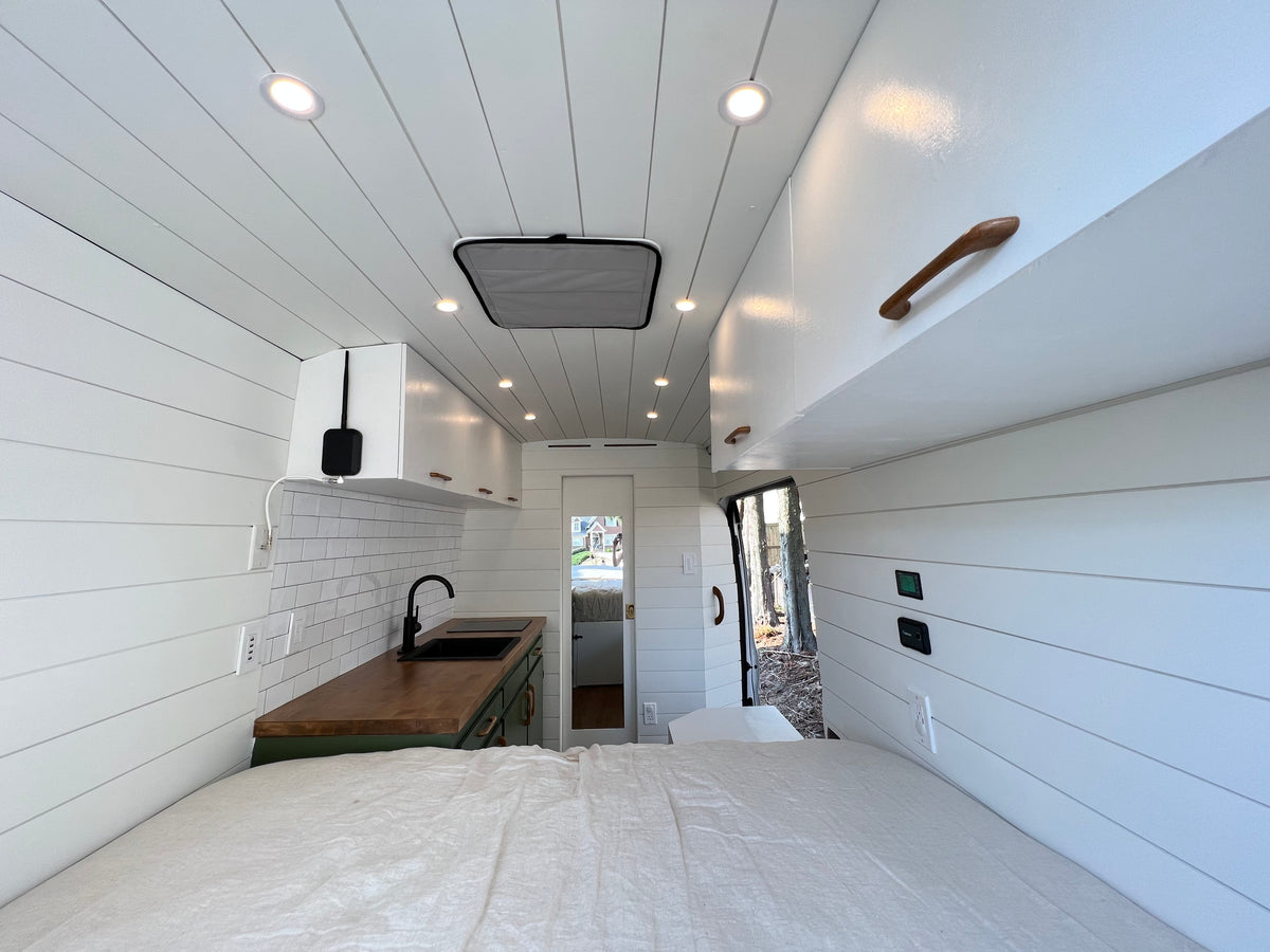 Modern rv rental interior showcasing a compact kitchen with wood counters, a comfortable bed, and clean white shiplap walls. — photo 4