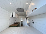 Modern rv rental interior showcasing a compact kitchen with wood counters, a comfortable bed, and clean white shiplap walls.